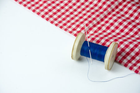 spool of thread and needle on a red checkered fabricの写真素材
