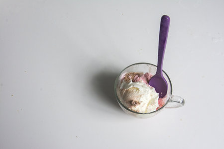 ice cream in a glass with purple spoon on a white background.
