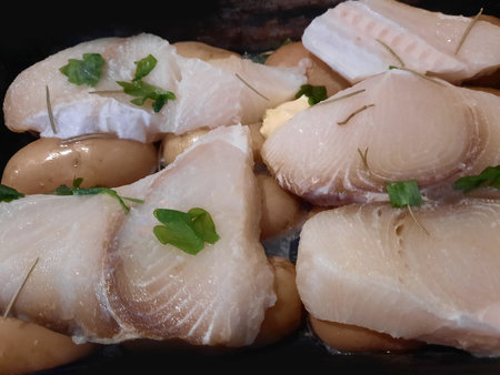 Fish fillets with butter and parsley on a black plate.