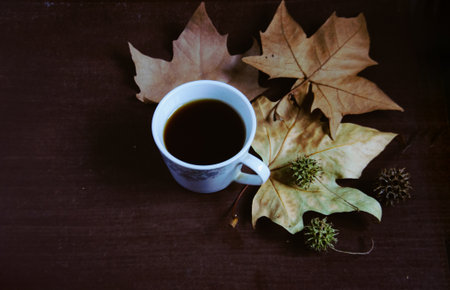 Coffee cup and autumn leaves on wooden table, vintage tone