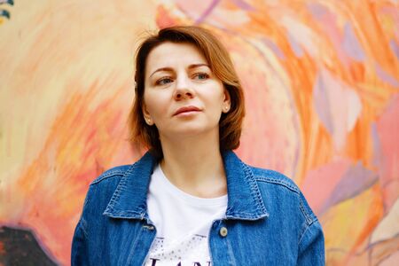 Beautiful thoughtful brown haired woman with blue eyes on colorful orange wall backround outdoorsの写真素材