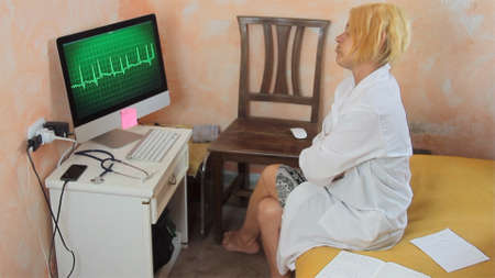 female doctor working in smart work from home reading an ECG cardiogram dressed in white shirts stethoscope and health mask and is desperateの写真素材
