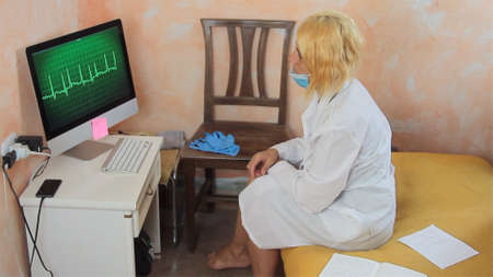 female doctor working in smart work from home reading an ECG cardiogram dressed in white shirts stethoscope and health mask and is desperateの写真素材