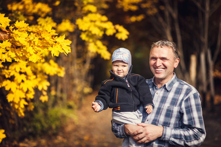 Active grandfather holding his grandchild, little toddler boy on arm, on sanny day, autumn. Happy, joyful familyの写真素材