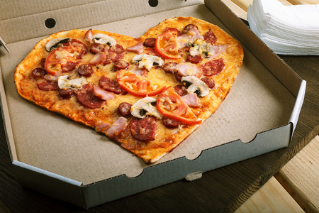 Pizza heart shape on dark wooden background top view. Thin pastry crust on wooden deskの写真素材