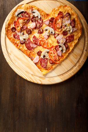 Pizza heart shape on dark wooden background top view. Thin pastry crust on wooden deskの写真素材