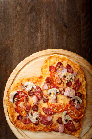 Pizza heart shape on dark wooden background top view. Thin pastry crust on wooden deskの写真素材