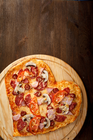 Pizza heart shape on dark wooden background top view. Thin pastry crust on wooden deskの写真素材