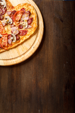 Pizza heart shape on dark wooden background top view. Thin pastry crust on wooden deskの写真素材