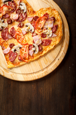 Pizza heart shape on dark wooden background top view. Thin pastry crust on wooden deskの写真素材