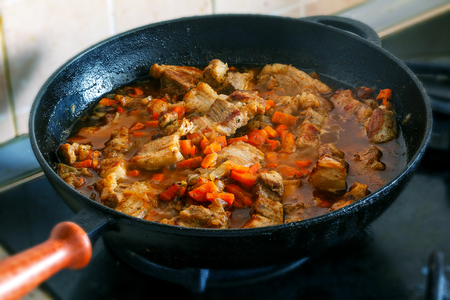 Cooking pork with carrot and onion on stoveの写真素材