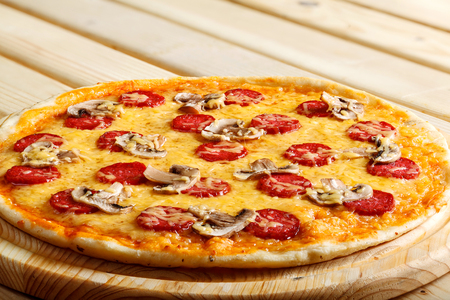 Delicious hot italian pizzas served on wooden table with tomato, mushrooms, garlic and pepperの写真素材