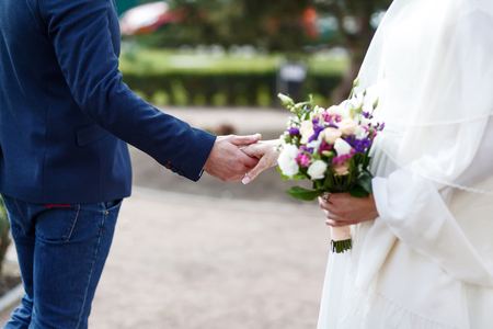 Detail of newlyweds, bride and groom, holding hands and flower bouquet, back view.の写真素材