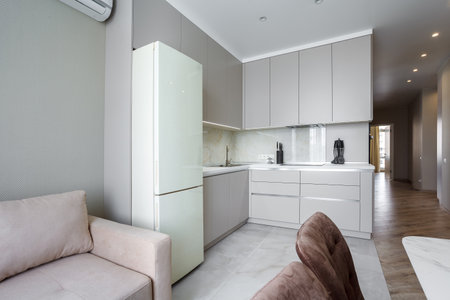 Modern beige and gray stylish kitchen with a table, soft chairs, a sofa and a beige refrigerator. Floor tiles and laminate. Built in household applianceの写真素材