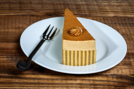 Caramel cake on plate with fork and wooden background