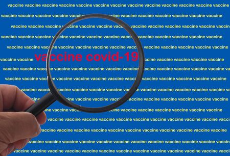 Hand with loupe searching for vaccine covid-19 in busy text backgroundの写真素材