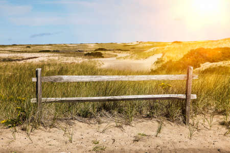 Fence with sand dunes view and blue sky with sun