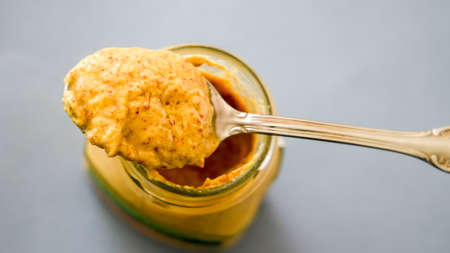 Mustard on spoon with blue background on glass jarの写真素材