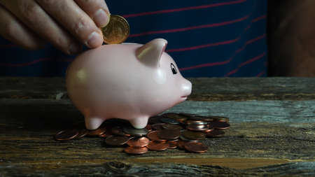 Hand is adding money inside pink piggy saving bankの写真素材