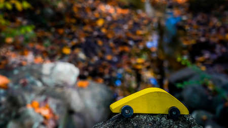 Wooden yellow toy car with autumn colored leaves in background with copy space