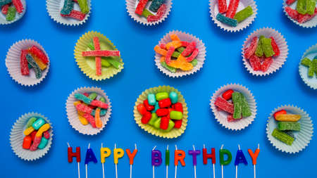 Various candy inside  baking cups on blue background with happy birthday textの写真素材