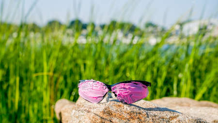 Pink covered sunglasses on rock with green grass on background and copy space
