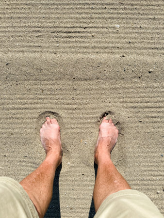 A person's bare feet standing on sandy beach