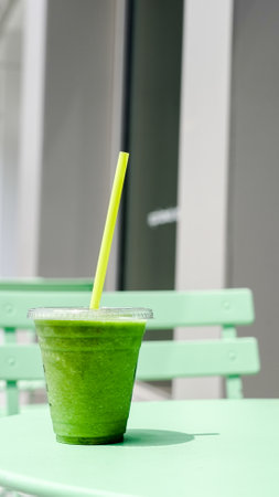 A vibrant green smoothie sits on a pastel green table outsideの写真素材