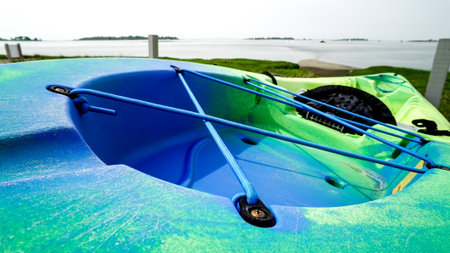 A vibrant kayak rests on the shore, featuring a blue and green design. Calm waters extend into the distance, offering a tranquil setting for paddling.の写真素材