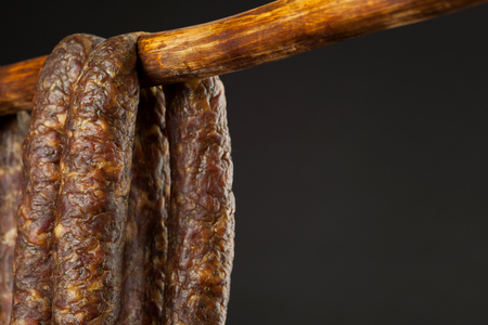 hanging smoked domestic traditional sausage on a stick on black backgroundの写真素材