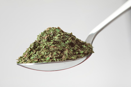 spoon of green dried herbs on white backgroundの写真素材