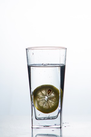 Glass glass of water with lemon on the isolated background. Mountain mineral pure mountain water with gas bubbles and a lemon slice and spray tonic refreshing sports drink.の写真素材