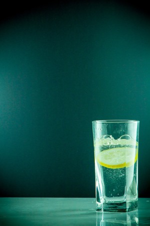 Glass glass of water with lemon on the isolated background. Mountain mineral pure mountain water with gas bubbles and a lemon slice and spray tonic refreshing sports drink.の写真素材