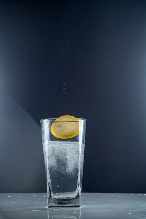 Glass glass of water with lemon on the isolated background. Mountain mineral pure mountain water with gas bubbles and a lemon slice and spray tonic refreshing sports drink.の写真素材