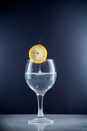 Glass glass of water with lemon on the isolated background. Mountain mineral pure mountain water with gas bubbles and a lemon slice and spray tonic refreshing sports drink.の写真素材