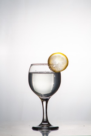 Glass glass of water with lemon on the isolated background. Mountain mineral pure mountain water with gas bubbles and a lemon slice and spray tonic refreshing sports drink.の写真素材