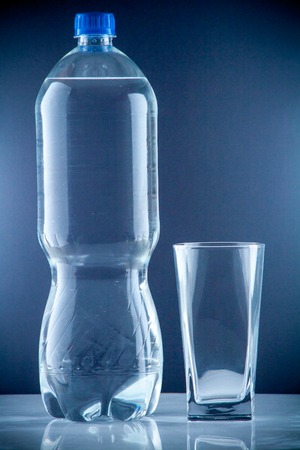 bottle of clear drinking cold mineral water with gas in isolation on the background next to a glass transparent glassの写真素材
