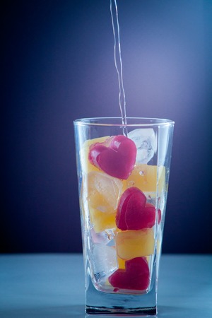 red heart of ice falling with splashes into a glass with a drink a cocktail of heartの写真素材