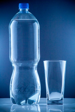 bottle of clear drinking cold mineral water with gas in isolation on the background next to a glass transparent glassの写真素材