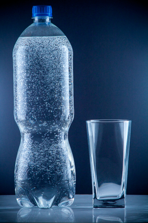 Pure mineral water pouring from a bottle into a glass. bottle of clear drinking cold mineral water with gas in isolation on the background next to a glass transparent glassの写真素材