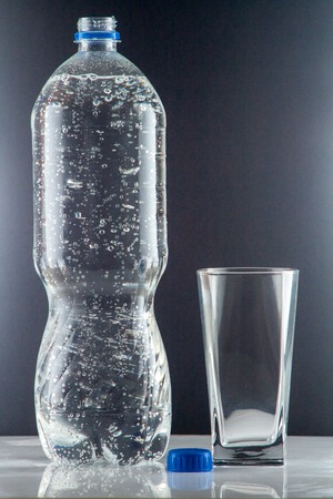 Pure mineral water pouring from a bottle into a glass. bottle of clear drinking cold mineral water with gas in isolation on the background next to a glass transparent glassの写真素材