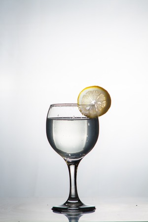 Glass glass of water with lemon on the isolated background. Mountain mineral pure mountain water with gas bubbles and a lemon slice and spray tonic refreshing sports drink.の写真素材