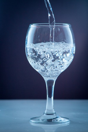 Clean drinking water from a source pouring into a clear glass beaker in the backgroundの写真素材