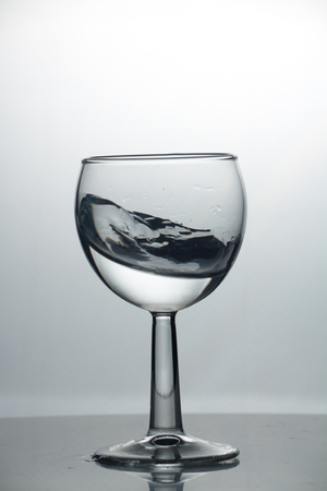 Transparent glass cup with a pouring bubbling cold fresh water with bubbles and dropsの写真素材