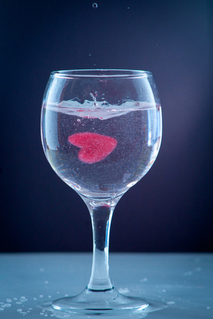 red heart of ice falling with splashes into a glass with a drink a cocktail of heartの写真素材