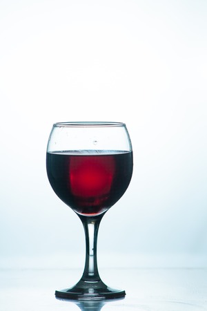 bright beautiful red wine pouring jet into a transparent glass cup isolated on a dark backgroundの写真素材