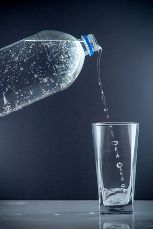 Pure mineral water pouring from a bottle into a glass. bottle of clear drinking cold mineral water with gas in isolation on the background next to a glass transparent glassの写真素材