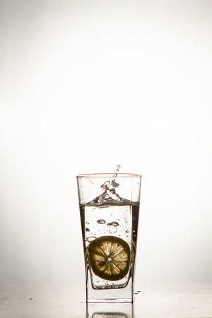 Glass glass of water with lemon on the isolated background. Mountain mineral pure mountain water with gas bubbles and a lemon slice and spray tonic refreshing sports drink.の写真素材