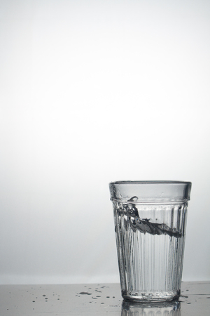 Transparent glass cup with a pouring bubbling cold fresh water with bubbles and dropsの写真素材