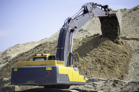 A large yellow excavator on the road construction site picks up and pours sand rubble stones in a quarry construction machinery excavator digsの写真素材